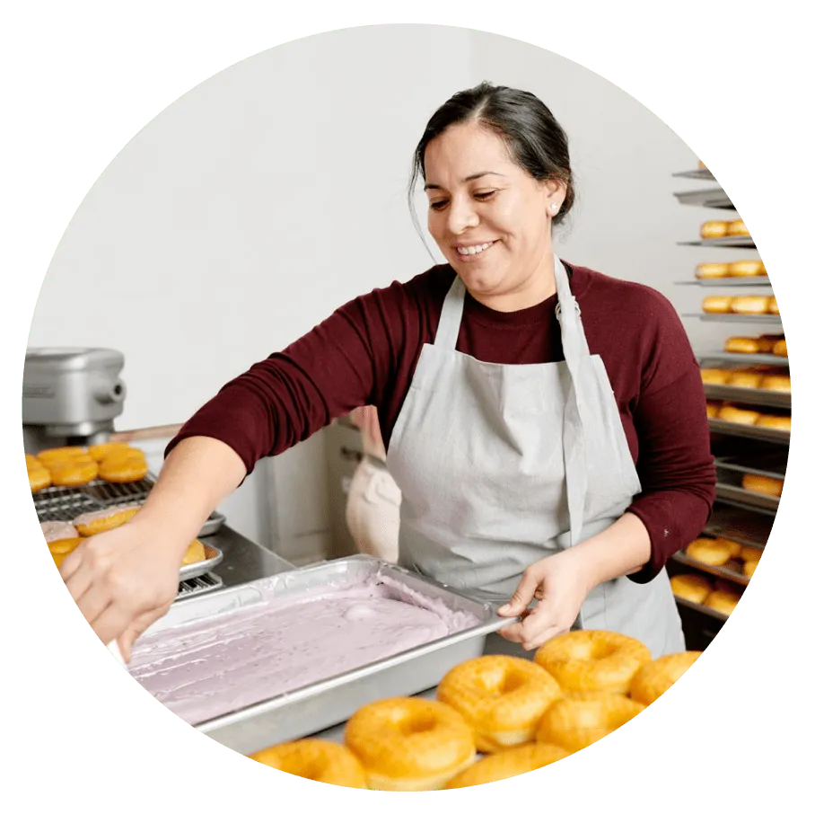 Hero image - Woman preparing the frosting for starting glazing a tray of donuts.
